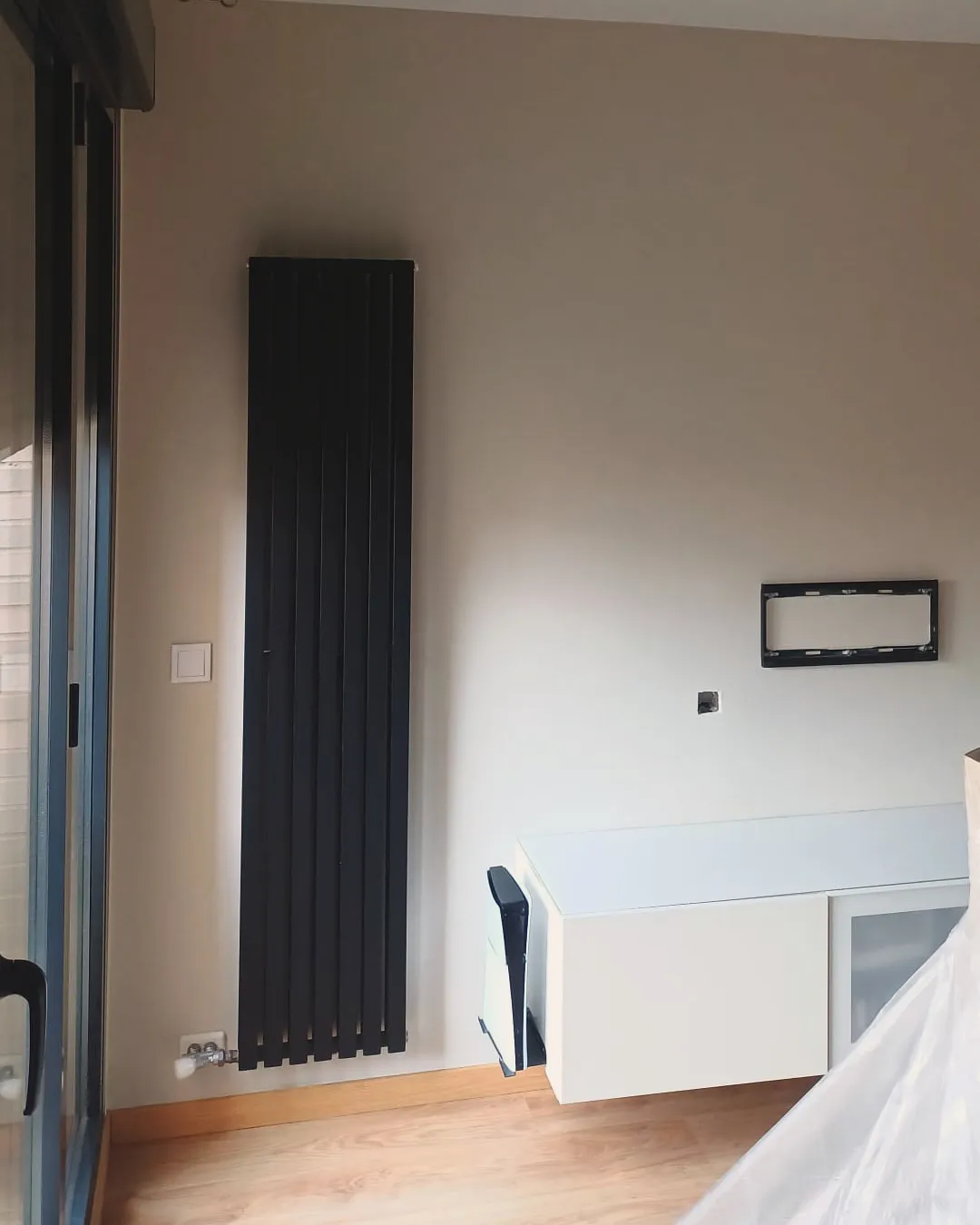Salón recién pintado con radiador vertical negro sobre pared lisa y suelo de madera