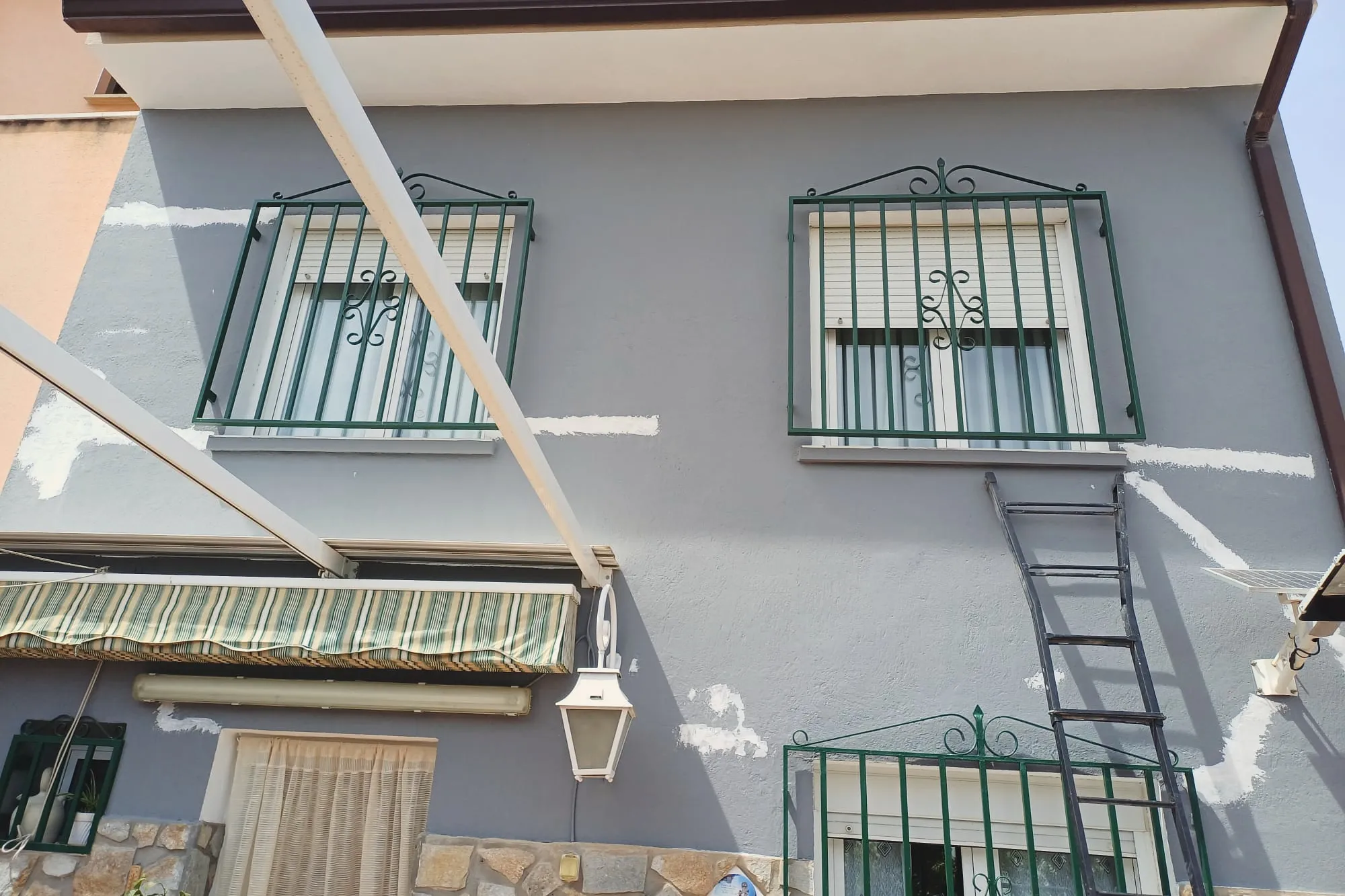 Fachada de vivienda en gris con zócalo de piedra y grietas selladas antes del acabado