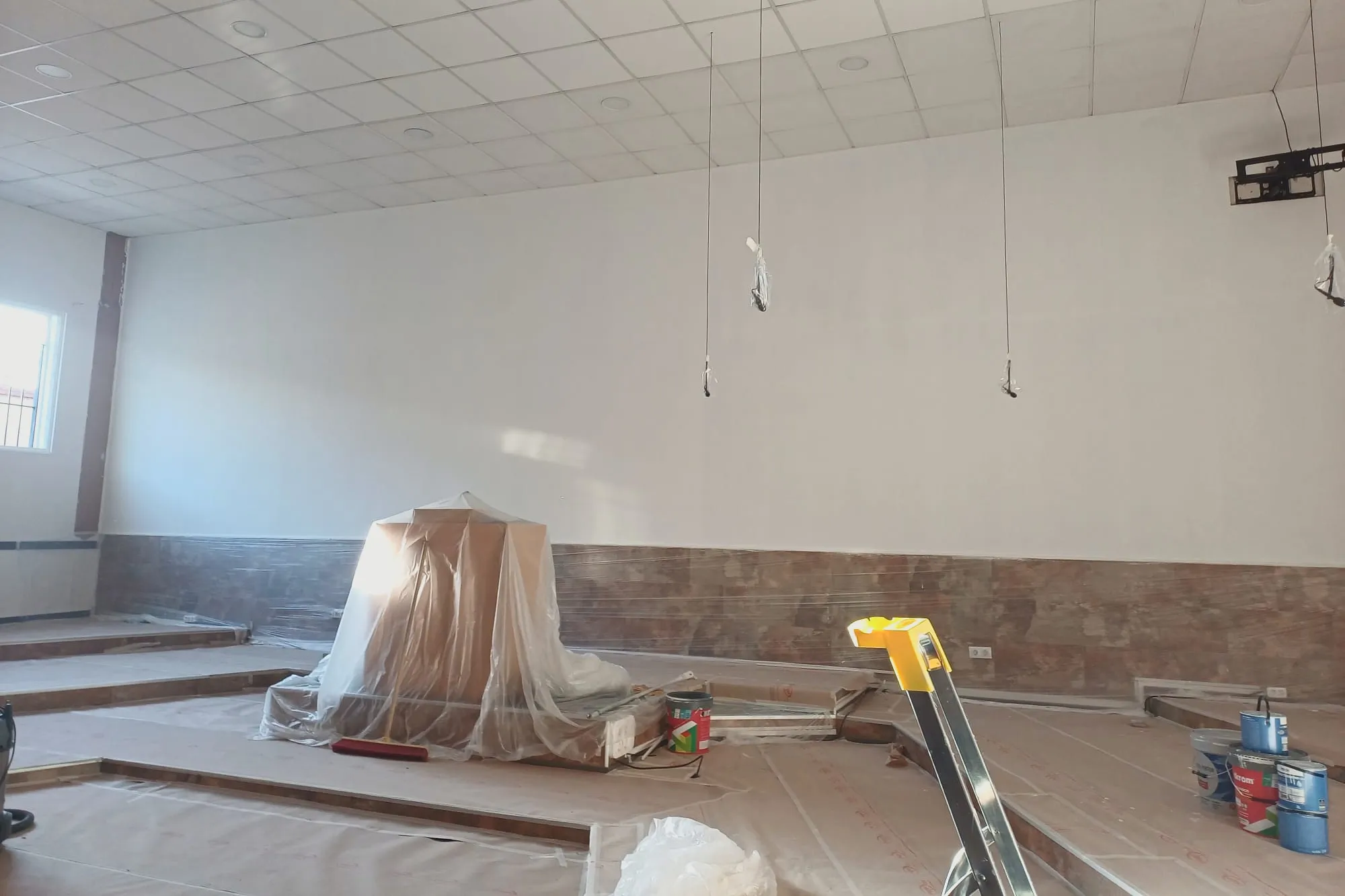 Sala amplia con suelos y mobiliario cubiertos, franja de estuco en la pared del fondo